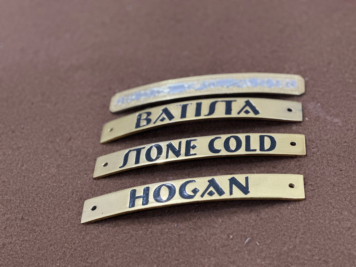 Four brass nameplates with engraved names on a brown surface