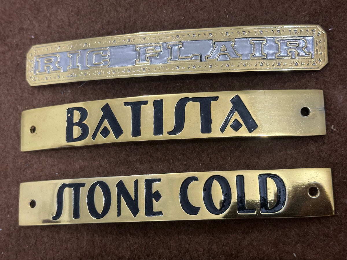 Three brass nameplates with engraved text on a brown background