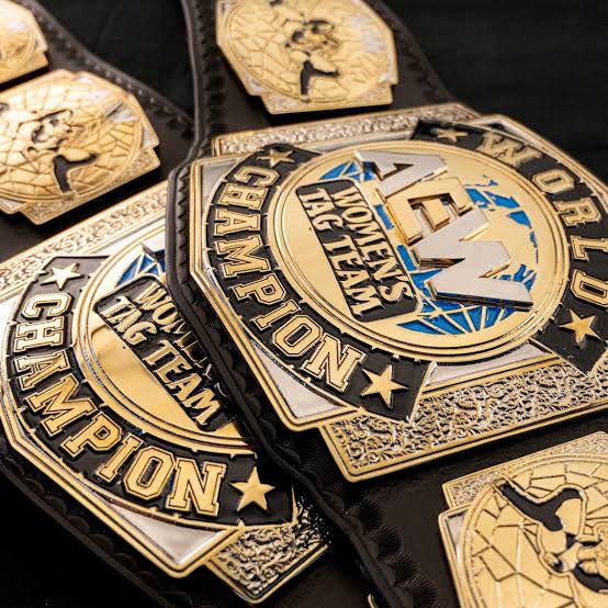 Close-up of a black and gold championship belt with multiple engraved plates, including one that reads 'WOMEN'S BIG TEAM' and 'CHAMPION.'.
