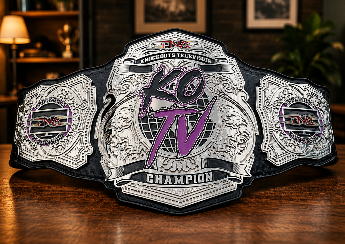 A championship belt with ornate silver-toned plates and purple 'KO TV' lettering, displayed on a wooden surface in a dimly lit indoor setting.