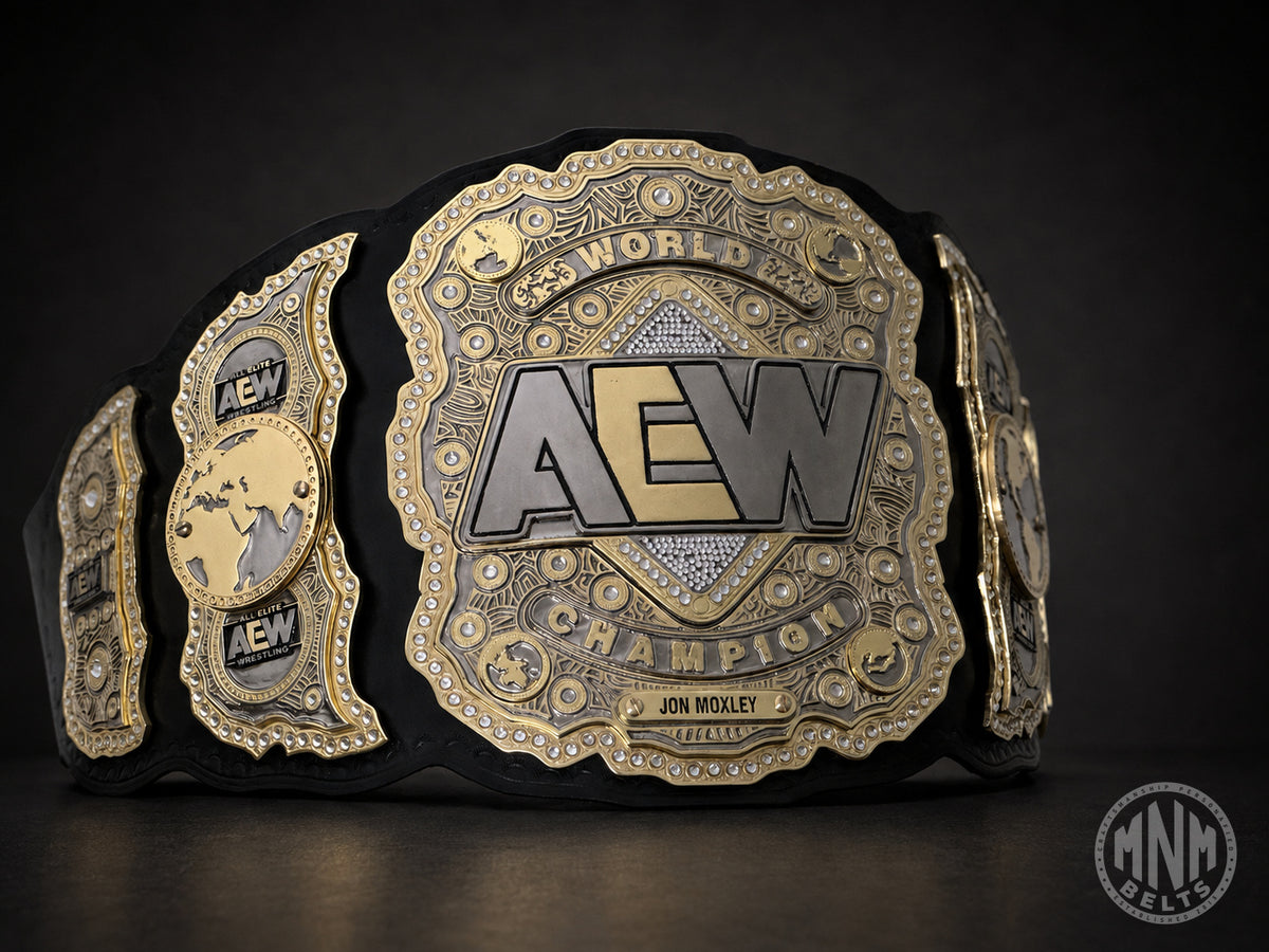 A black and gold AEW World Champion belt with ornate metallic plates and the name Jon Moxley on the front, photographed against a dark studio background.