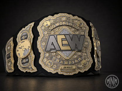 A black and gold AEW World Champion belt with ornate metallic plates and the name Jon Moxley on the front, photographed against a dark studio background.