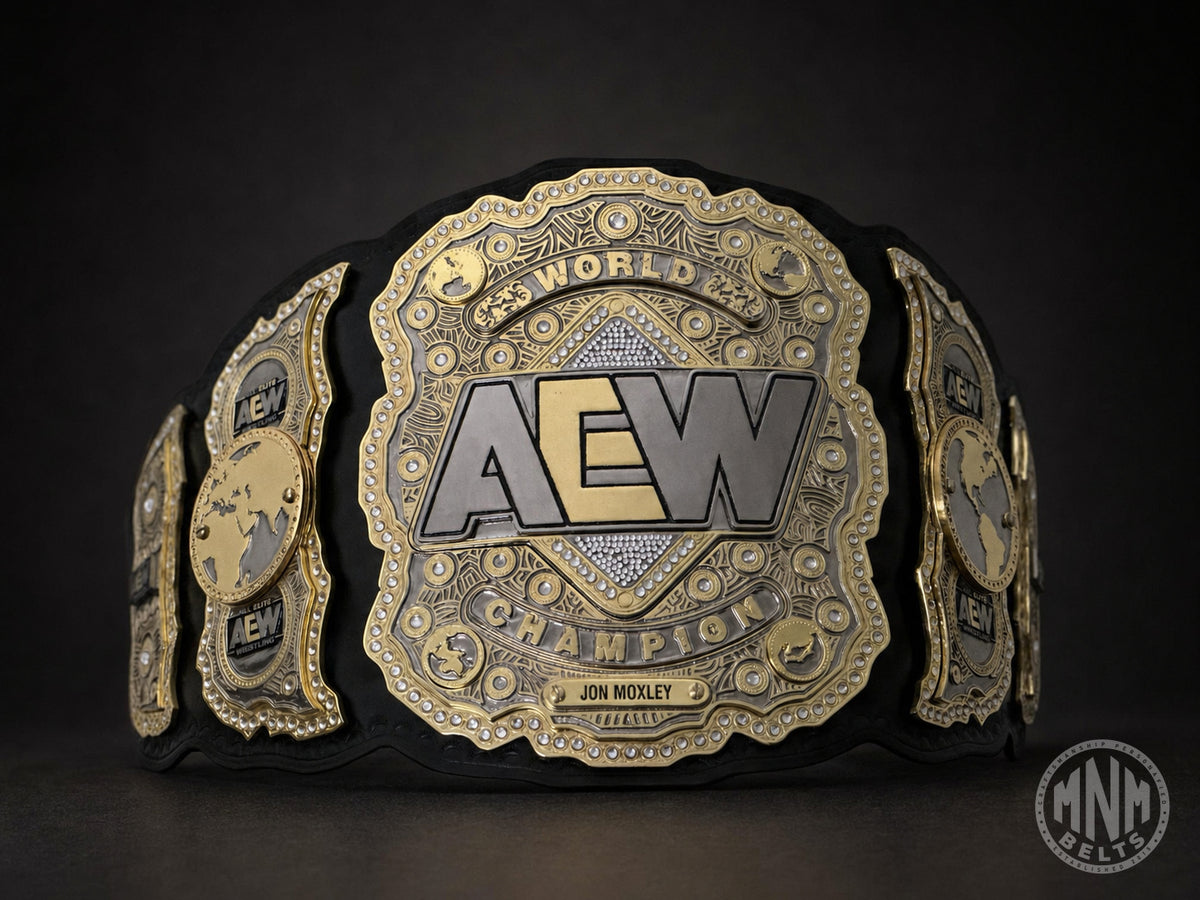 A close-up studio shot of a championship belt with a large central AEW World Champion plate, flanked by two smaller side plates, photographed against a dark background.