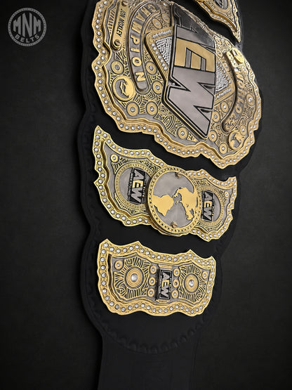 A close-up of a black championship belt with ornate gold and silver plates featuring the AEW logo and intricate detailing, set against a dark background.